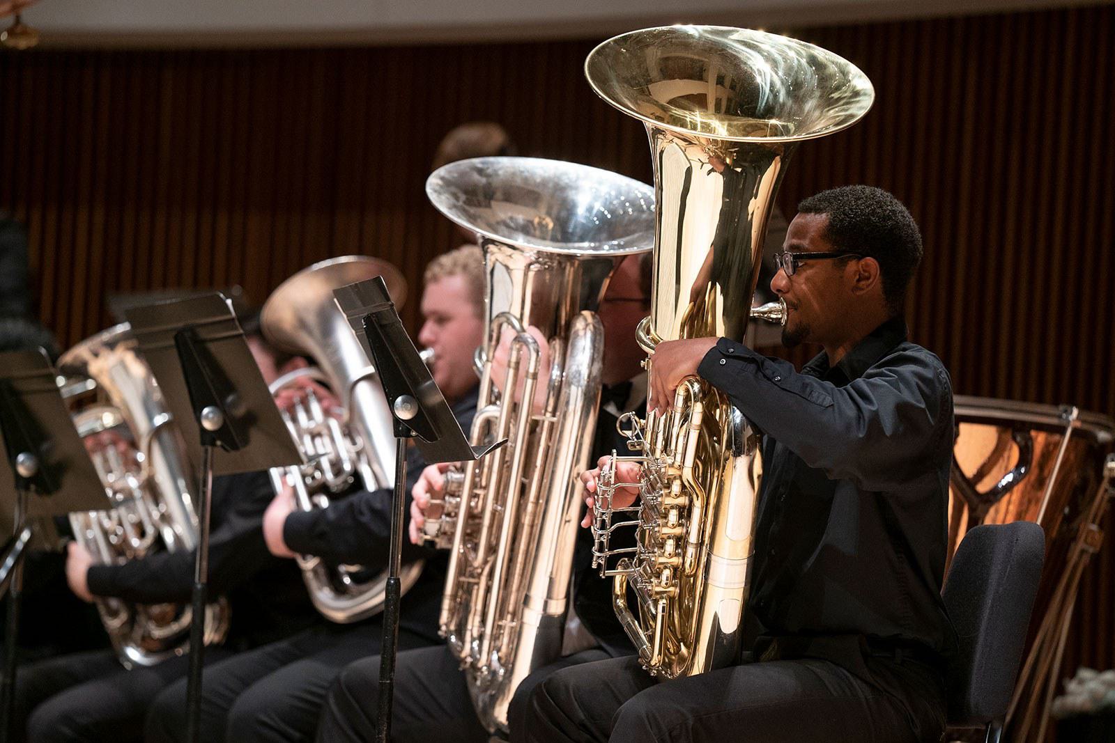 Men wearing black clothing play tubas on stage.