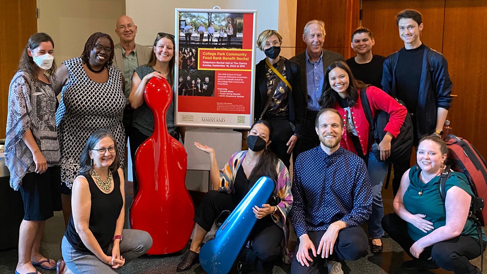 A group of people pose for a picture around an event poster.