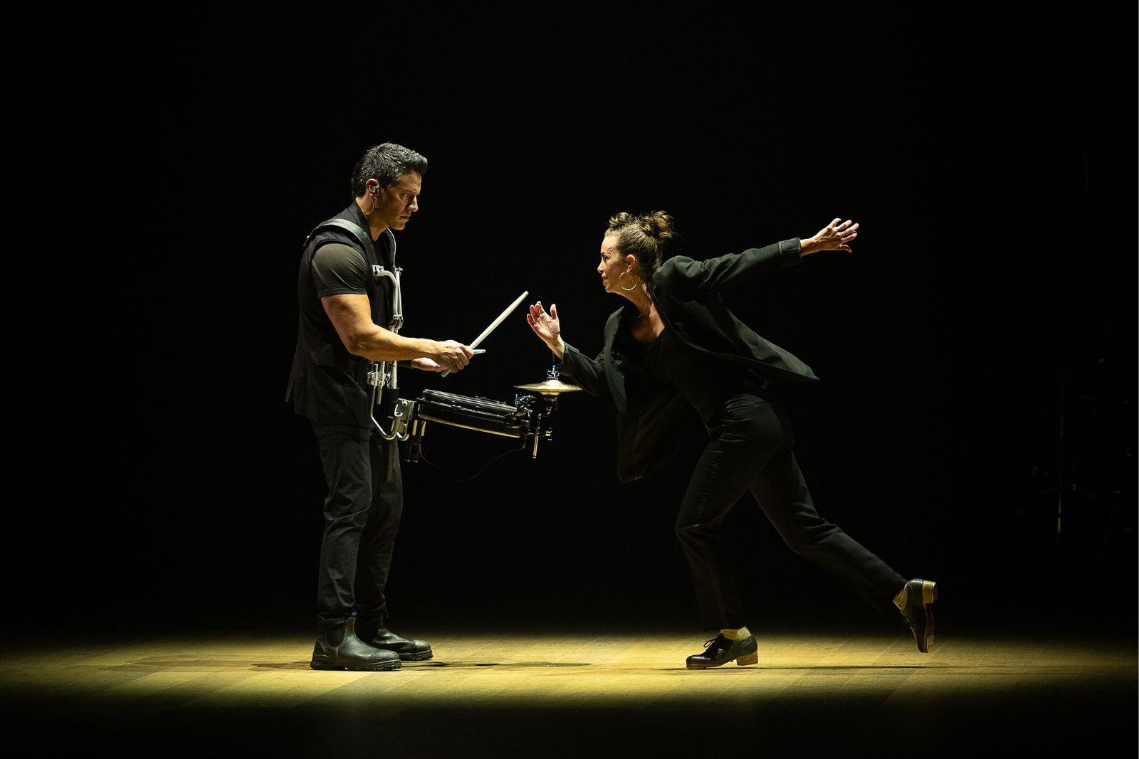 A tap dancer and percussionist perform together on stage.