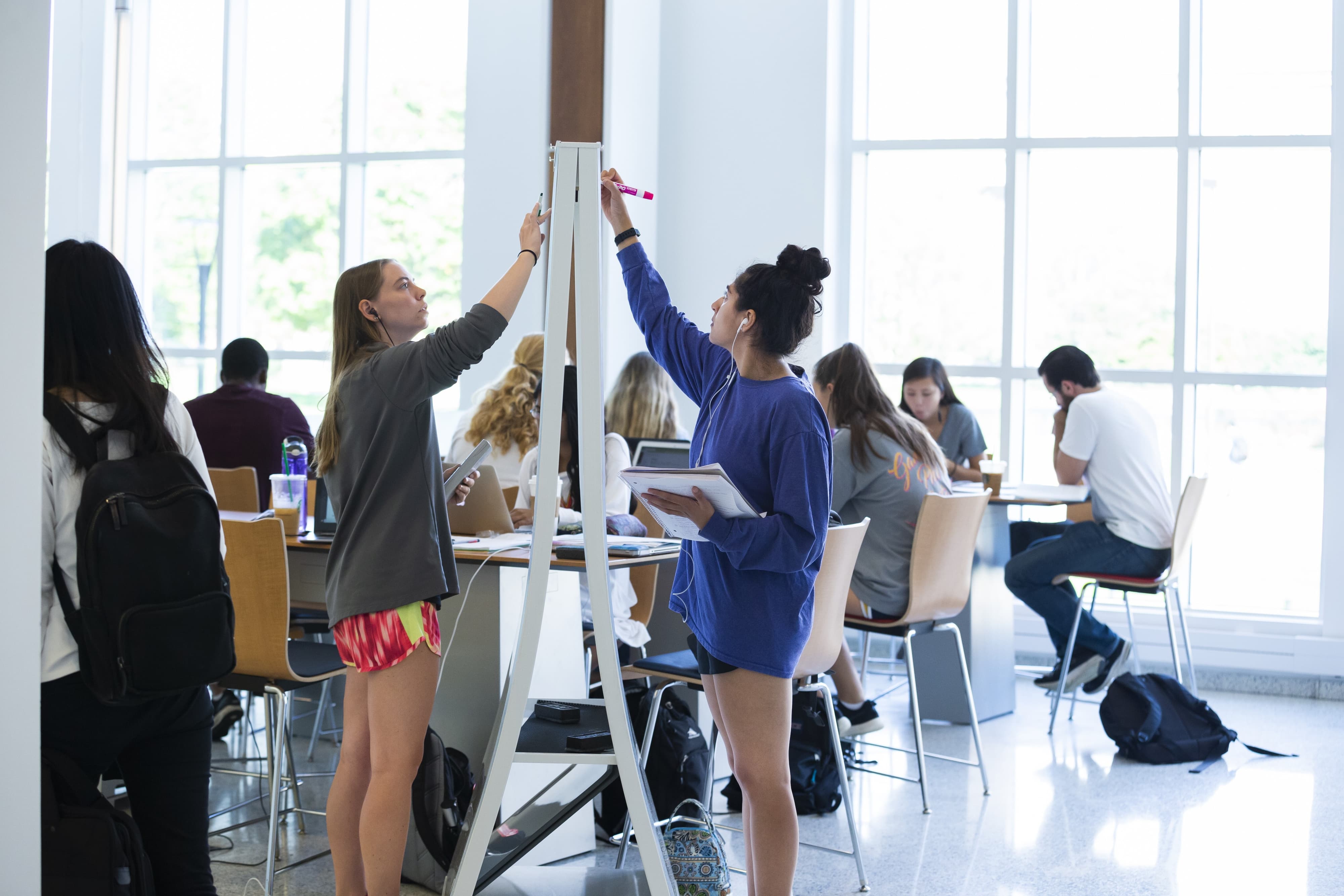 Two students writing on a white board