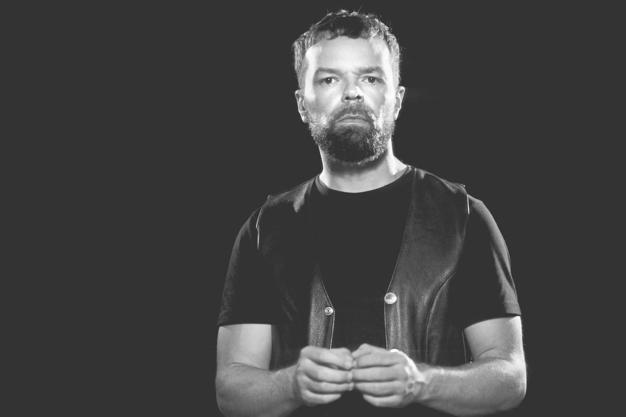 Man poses for a black and white picture against a black background.