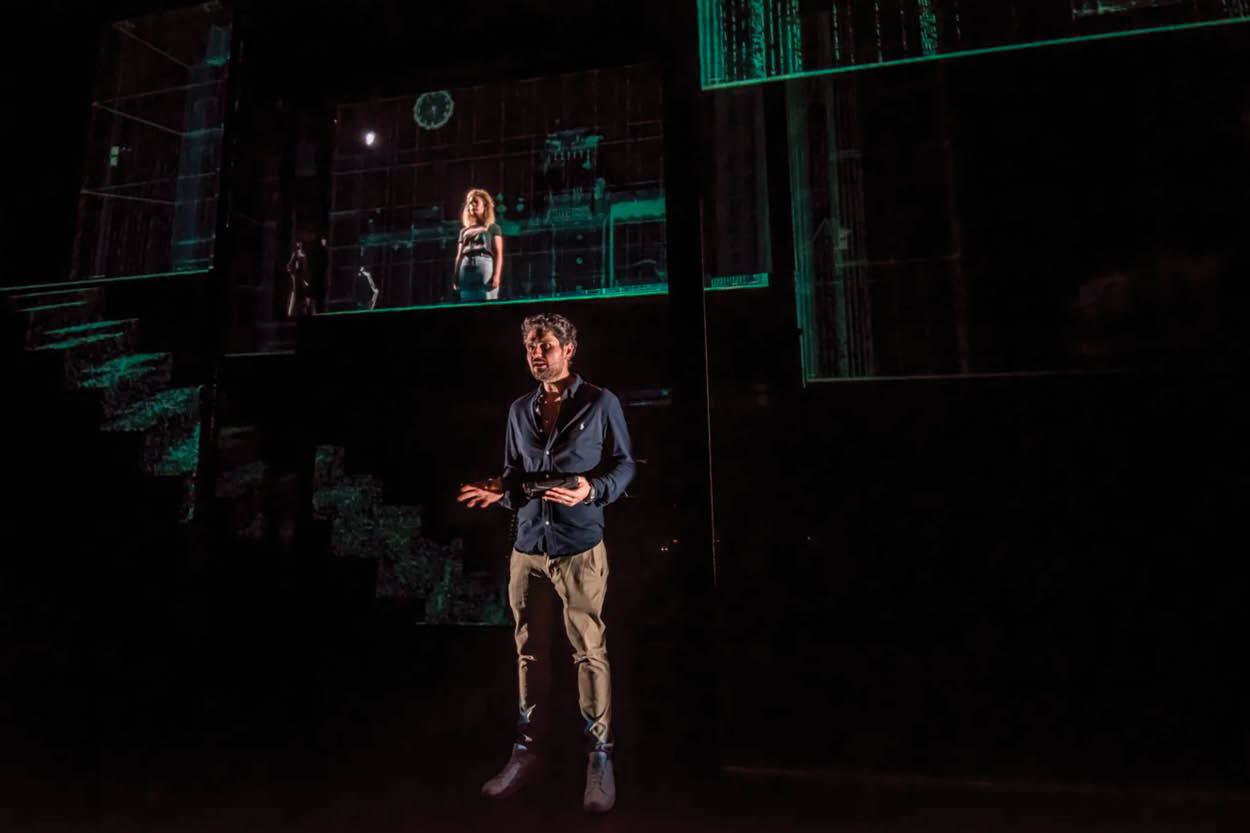 A man and woman stand on a dark stage.