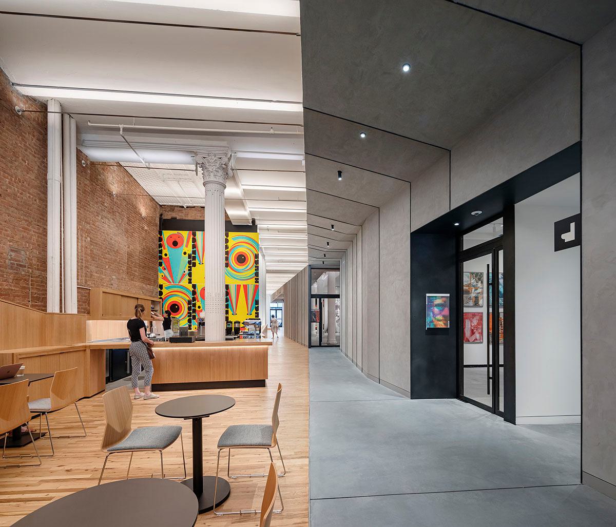 Split image of interior of a building, the left side is has wooden furniture, a brick and a colorful wall division. The right side is grey concrete.