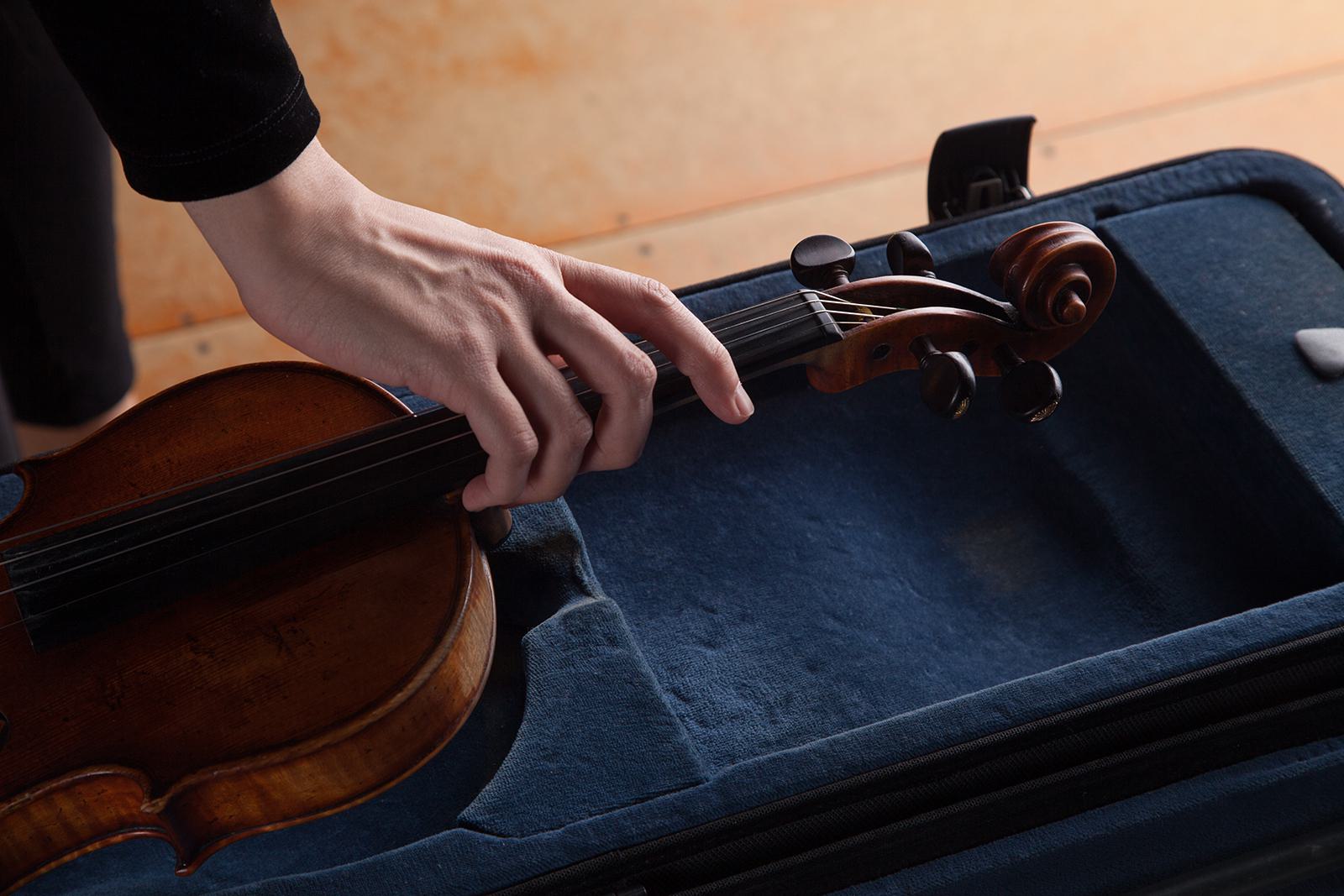 A person's hand picks up a violin out of its case.