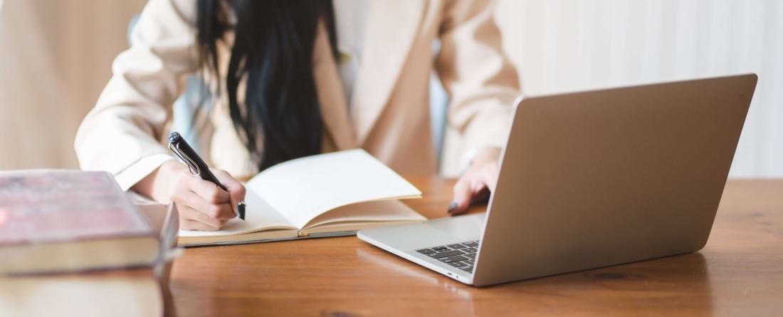 Woman working on laptop and writing in notebook