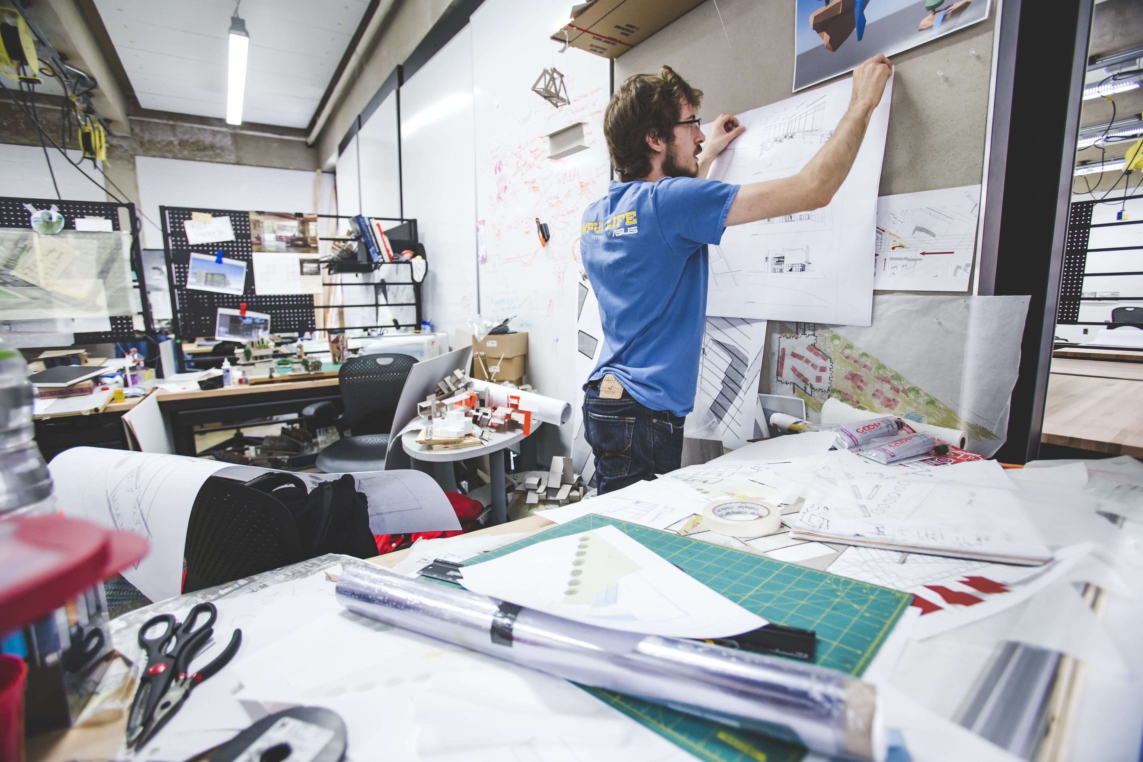 Architecture student pinning plans to board with work in the foreground
